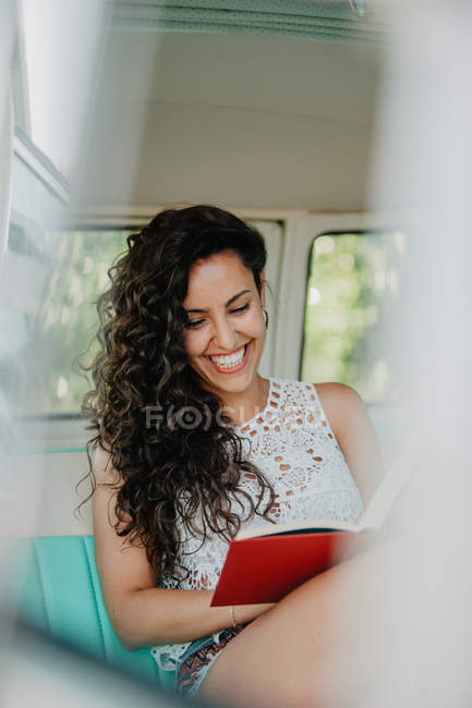Усміхнена молода жінка сидить всередині каравана і читає книгу — стокове фото