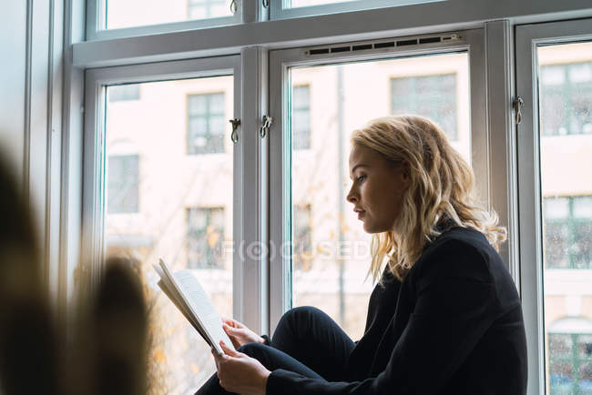 Sogno donna lettura libro mentre seduto sul davanzale della finestra a casa — Foto stock