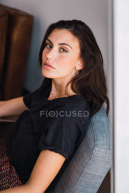 Jeune femme brune sensuelle assise dans un fauteuil et regardant la caméra — Photo de stock