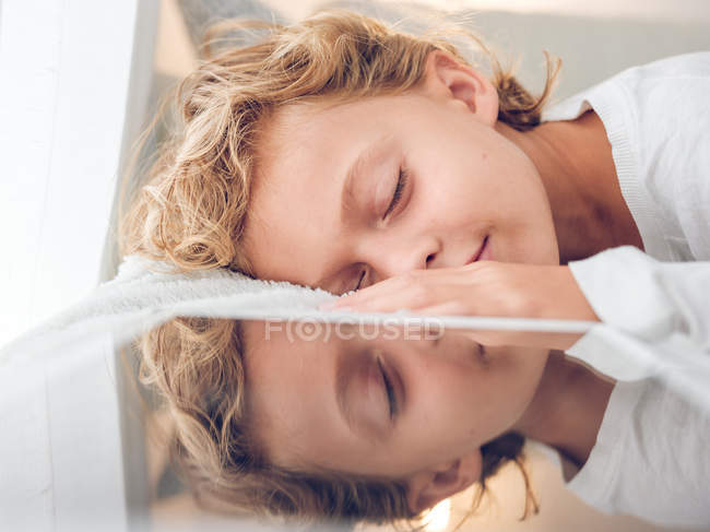 Mignon garçon avec les cheveux bouclés couché près tablette numérique avec les yeux fermés — Photo de stock