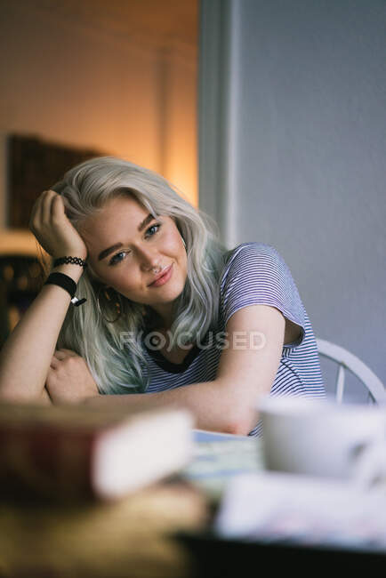 Красивая молодая женщина расслабляется и смотрит в камеру, сидя дома. — стоковое фото
