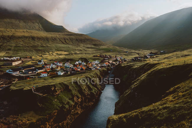 Vista de un pequeño pueblo en grandes montañas verdes en las Islas Feroe - foto de stock