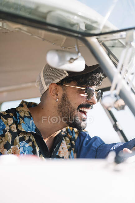 Вид збоку красивого молодого чоловіка в стильному вбранні, що сидить на сидінні водія і рульовому ретро фургоні під час подорожі — стокове фото