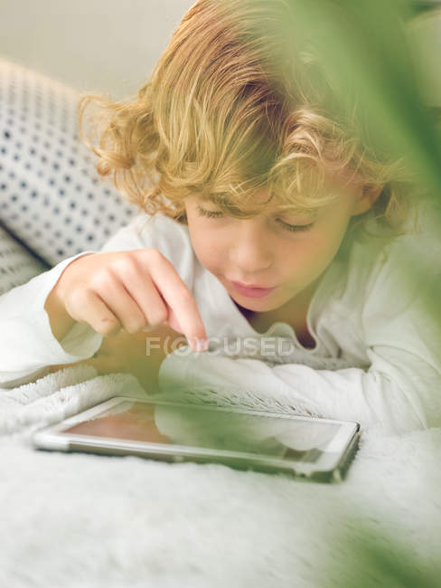 Хлопчик натискає екран цифрових планшетів, лежачи на зручному дивані — стокове фото