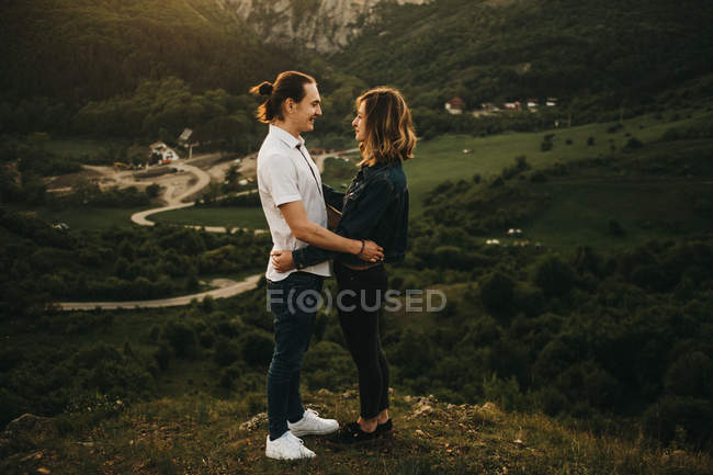 Мила пара обіймається, стоячи на тлі красивої долини і гір — стокове фото