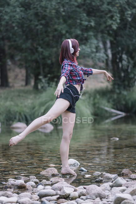 Red haired girl performs exercises by the river — Stock Photo