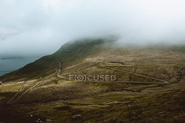 Estrada rural torta em montanhas verdes em nuvens nas Ilhas Feroé — Fotografia de Stock