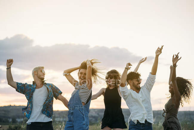 Groupe de jeunes en tenue décontractée riant et dansant tout en s'amusant dans une belle campagne ensemble — Photo de stock