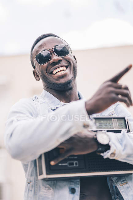 Улыбающийся черный мужчина в солнцезащитных очках держит винтажное радио устройство — стоковое фото