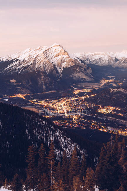 View from height of snowy mountain range with glowing city far away in valley below — Stock Photo