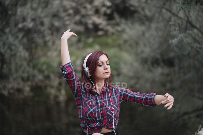 Menina de cabelos vermelhos ouve música junto ao rio — Fotografia de Stock