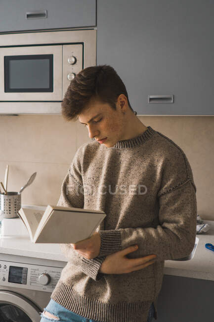 Casual homem leitura livro na cozinha — Fotografia de Stock