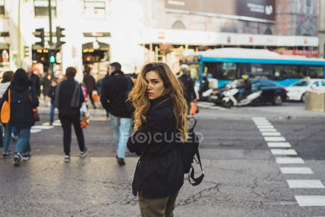 Молода жінка з рюкзаком озирається назад під час прогулянки по міській дорозі — стокове фото