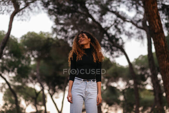 Da sotto vista di bella? ridendo? Afroamericana giovane donna con gli occhi chiusi in jeans e maglione nero su sfondo sfocato — Foto stock