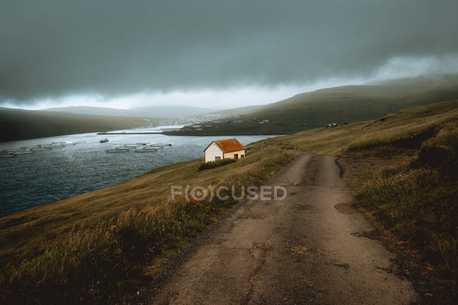 Petite maison grunge avec toit rouillé sur la rive du lac sur les îles Feroe par temps nuageux — Photo de stock