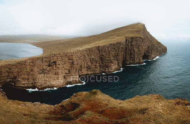 Oceano e penhasco rochoso sob céu nublado nas Ilhas Feroé — Fotografia de Stock