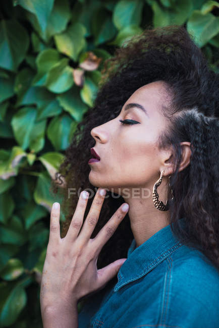 Sensual African American woman standing against green foliage — Stock Photo