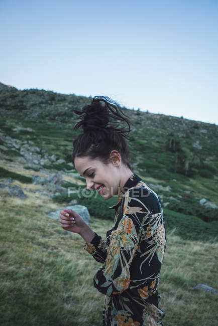 Giovane donna ridente in abito elegante fantasia in piedi vicino collina verde — Foto stock