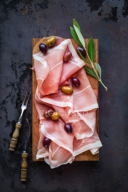 Prosciutto ham with olives on wooden cutting board — Stock Photo