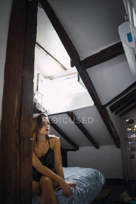 Femme sensuelle pensive assise sur le lit à la maison et regardant ailleurs — Photo de stock