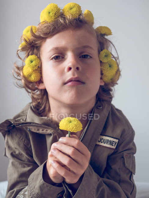 Garçon avec des fleurs dans les cheveux faisant des visages sur fond gris — Photo de stock