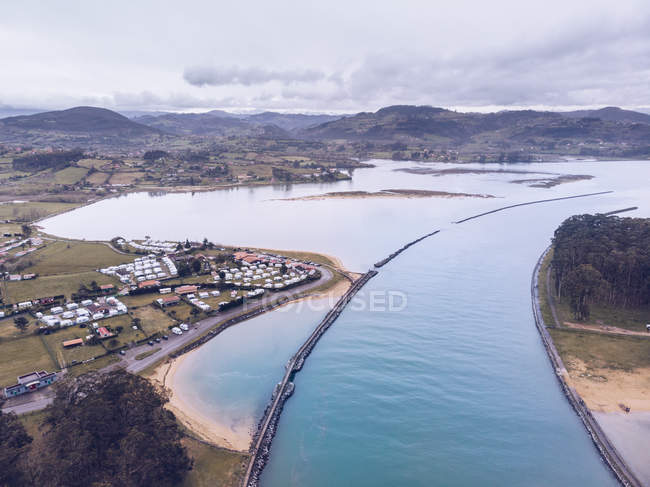 Panorama mozzafiato drone del fiume calmo che scorre vicino ai campi agricoli e piccolo insediamento nella giornata nuvolosa nelle Asturie, Spagna — Foto stock