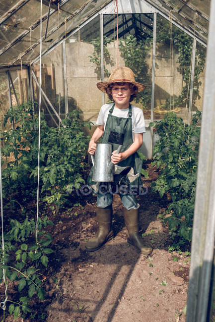 Boy standing with watering can in greenhouse — Stock Photo