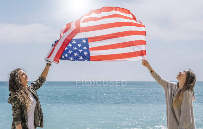 Due ragazze in posa sulla spiaggia con bandiera USA. — Foto stock