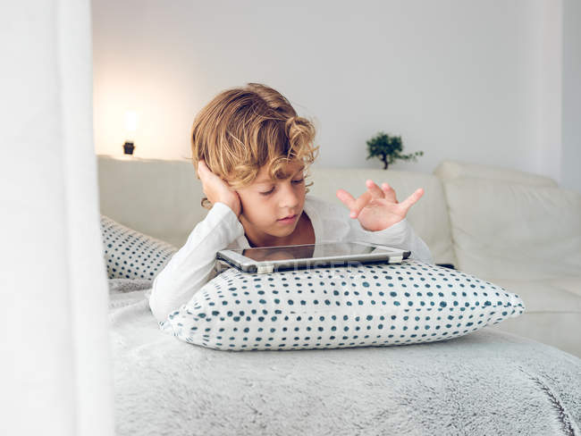 Menino usando tablet digital enquanto deitado no sofá em casa — Fotografia de Stock