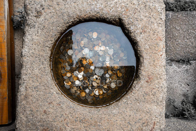 From above small well in rock with colorful coins placed in water — Stock Photo