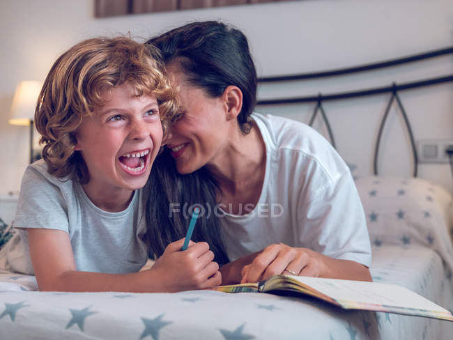 Hermosa mujer y lindo niño acostado en la cama cómoda y para colorear imágenes en cuaderno juntos - foto de stock