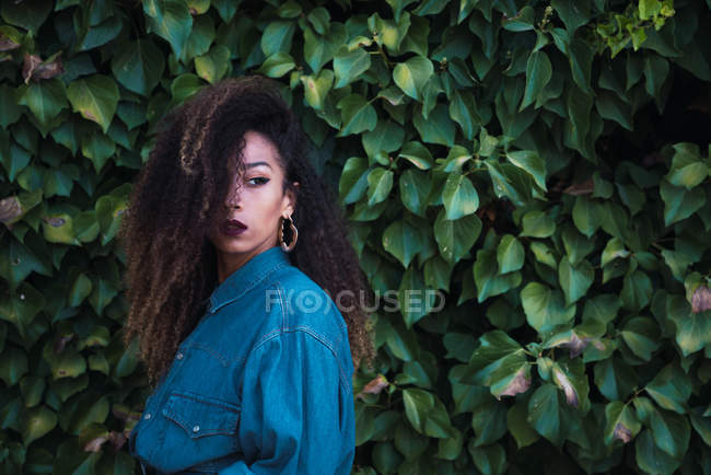 Confident African American woman standing against green foliage — Stock Photo