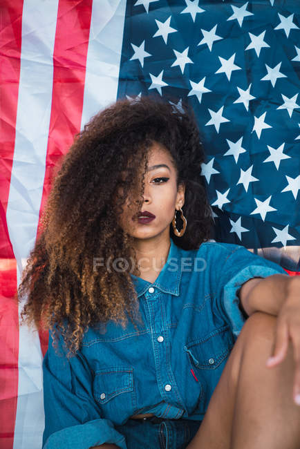 Junge Frau in Jeanskleidung sitzt vor der Flagge Amerikas — Stockfoto