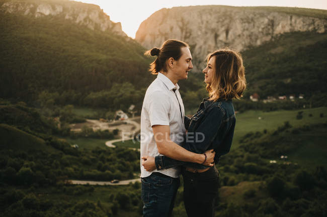 Nettes Paar, das sich umarmt und die Stirn zusammenbeißt, während es vor dem Hintergrund des wunderschönen Tals und der Berge steht — Stockfoto