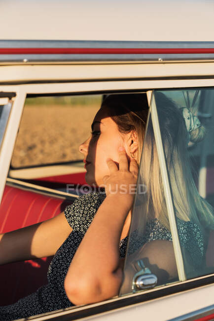 Jeune femme assise sur le siège conducteur et volant van vintage tout en voyageant dans la campagne par une journée ensoleillée — Photo de stock