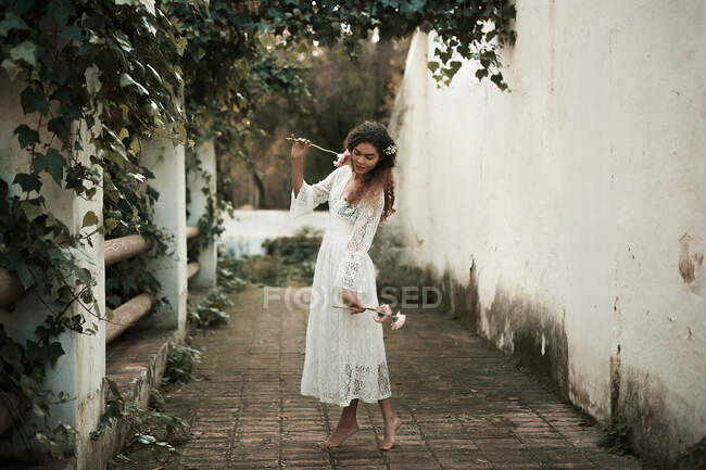 Vue latérale de belle afro-américaine pieds nus jeune dame en belle robe tenant des fleurs debout sur la pointe des pieds dans la cour — Photo de stock