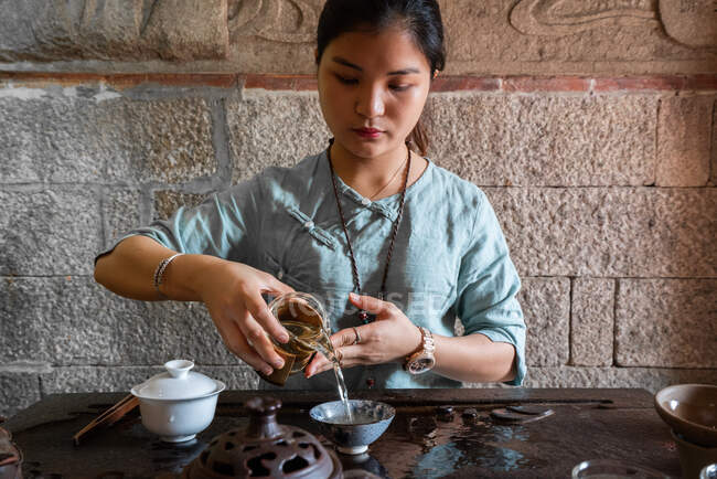 Jovem mulher asiática derramando água da panela enquanto faz chá na cerimônia tradicional — Fotografia de Stock