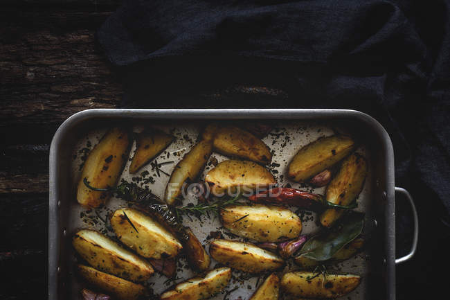 Cuñas de patata crujientes doradas tostadas en bandeja para hornear sobre mesa de madera - foto de stock