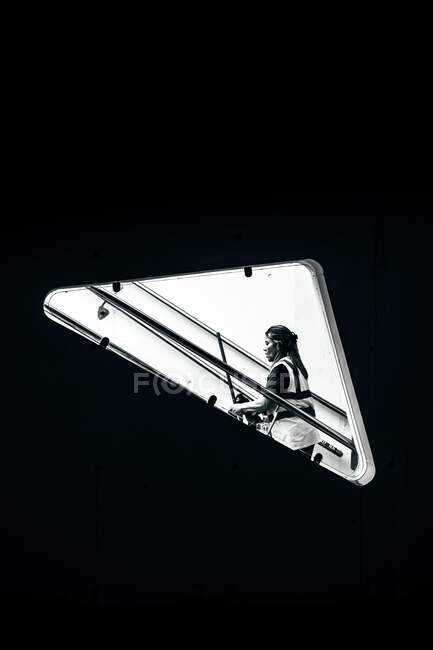Black and white shot of beautiful female carrying object and walking up steps behind triangle window — Stock Photo