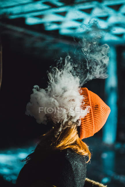 Seitenansicht einer nicht wiederzuerkennenden Frau, die Dampf pustet, während sie nachts in einem verlassenen Gebäude raucht. — Stockfoto