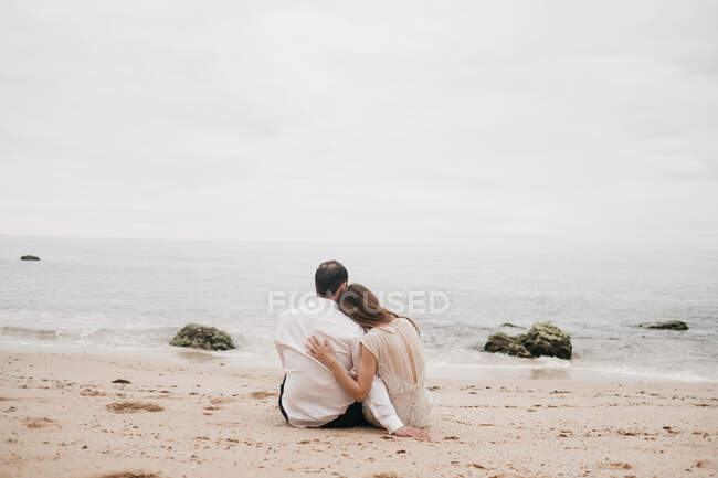 Newlyweds sitting on sand of ocean — Stock Photo