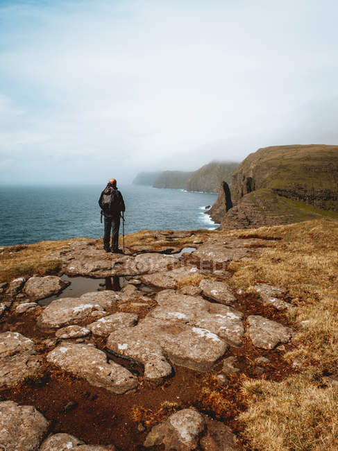 Unrecognizable hiker man standing on coast with stick and looking at ocean on Feroe Islands — Stock Photo