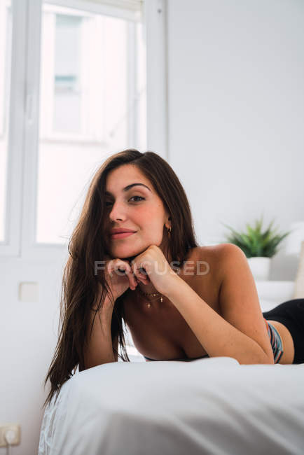 Jovem mulher morena alegre deitada na cama e olhando para a câmera — Fotografia de Stock
