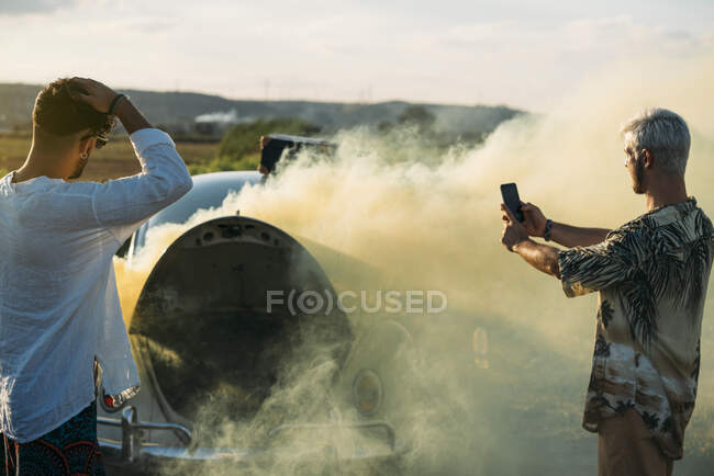Чоловік фотографує біля друга і зламану машину — стокове фото