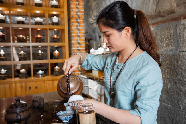 Jovem mulher asiática derramando água da panela enquanto faz chá na cerimônia tradicional — Fotografia de Stock