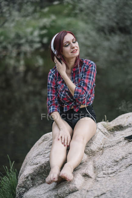 Червоне волосся дівчина слухає музику на річці — стокове фото