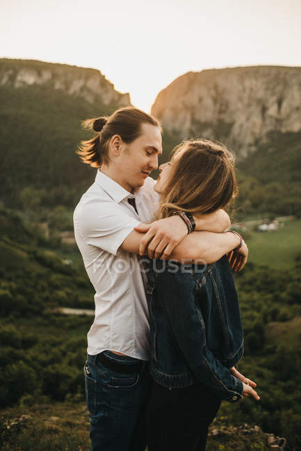 Nettes Paar, das sich umarmt und die Stirn zusammenbeißt, während es vor dem Hintergrund des wunderschönen Tals und der Berge steht — Stockfoto