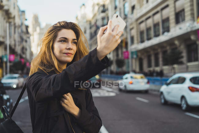 Woman taking selfie with smartphone on road in city — Stock Photo