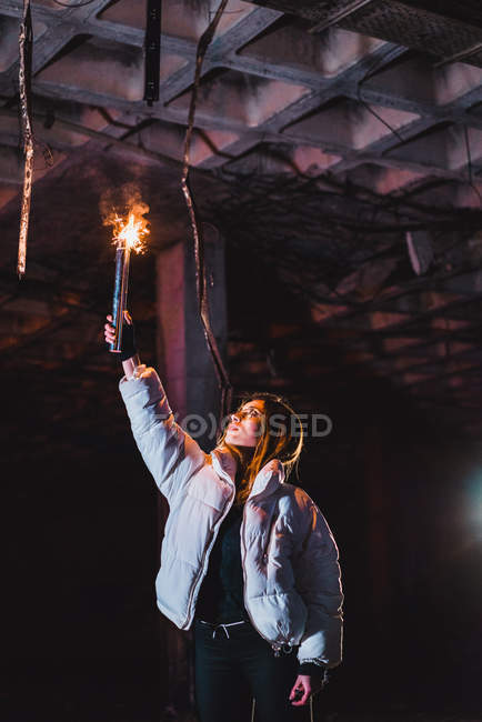 Pretty young woman standing with blazing torch in abandoned building at night. — Stock Photo