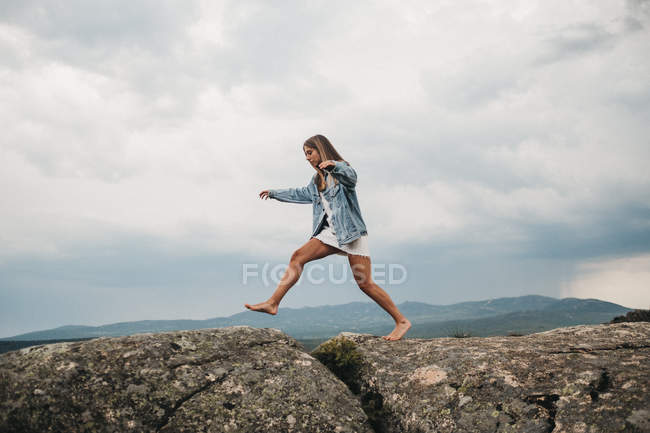 Mujer saltando sobre la grieta en las piedras - foto de stock